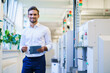 © BELLEVUE/Westend61 - Smiling male engineer holding digital tablet while standing by machinery at illuminated factory