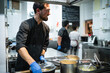 © SERGIO NIEVAS/Westend61 - Smiling chef working with coworker taking orders in background at kitchen