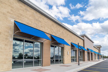 Brand New No Logo, Signage Or Label Storefront Of A Under Construction Strip Mall In The USA With Blue Awnings Above The Entrance, Blue Cloudy Sky Reflecting On The Windows