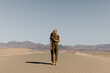 © Nicole Mason/Stocksy - young woman in fashionable green jumpsuit and hat standing on sand dunes with mountains in background
