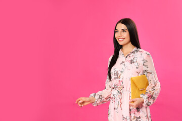Wall Mural - Young woman wearing floral print dress with elegant clutch on pink background. Space for text