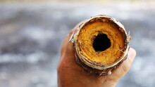 Old Water Pipes Clogged. Man's Hands Held Corroded Metal Plumbing And Blocked The Passage Of Water With Rust Forming Inside The Pipe. On A Cement Patio Background With A Copy Space. Selective Focus