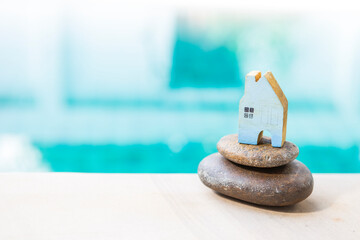 Wall Mural - Blue wooden house model on stack of stone over blurred blue water background, property business concept, new house