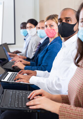 Wall Mural - Confident hispanic businessman in protective mask sitting with laptop in row with colleagues during business training. Precautions during mass events in coronavirus pandemic concept