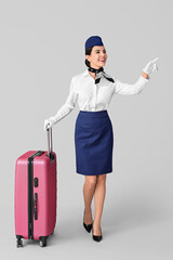 Wall Mural - Beautiful stewardess with luggage on grey background