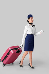 Poster - Beautiful stewardess with luggage on grey background