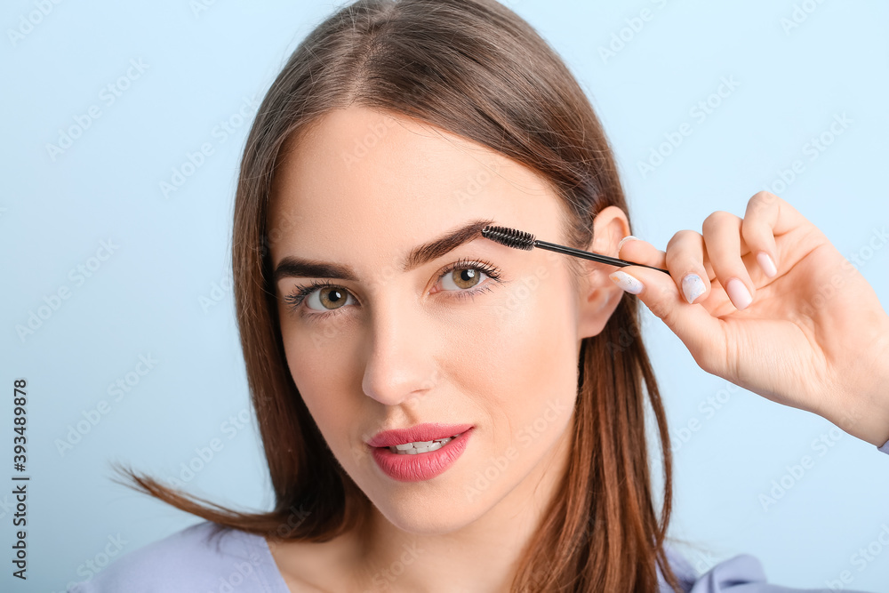 Young woman undergoing eyebrow correction procedure on color background