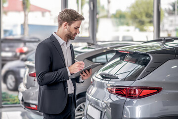 Wall Mural - Bearded male examining car boot, taking notes in the showroom