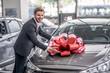 © zinkevych - Smiling brown-haired male putting red bow on car hood