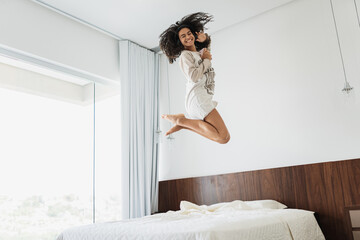 Wall Mural - curly hair latin american woman jumping on bed listen music