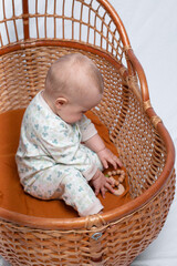 Wicker old cradle for a sleeping baby on a white background. The baby sits sideways in the cradle.