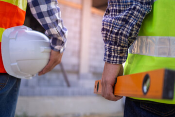 Professional engineers and builders in work clothes with tools and holding white helmets while standing outside the construction site.