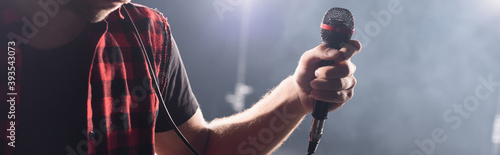 Fotomural Cropped view of vocalist of rock band holding microphone on blurred background,