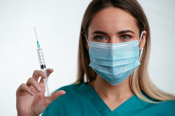 Beautiful female doctor with medical mask. Portrait of nurse with syringe in her hand.