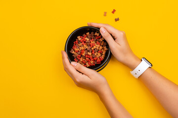 Human hands holding black color dog plate with dog dry crunchies in form of bone. Crunchy natural puppy treats and nutrition. Text space. Mustard color