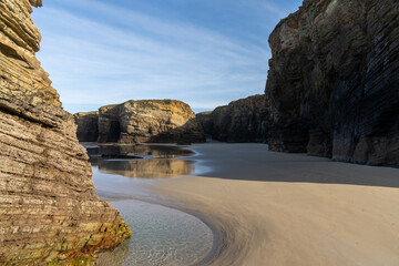 Sticker - sandy beach with tidal pools and jagged broken cliffs behind in warm evening light