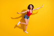 © deagreez - Full size photo of lovely dreamy young girl raise hands leg lips send air kiss attract guys party wear red singlet unclothed shoulders denim shorts isolated vibrant yellow color background