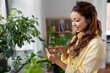 © Syda Productions - technology, people and internet concept - happy smiling asian woman with smartphone and flowers at home