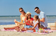 © Syda Productions - family, leisure and people concept - happy mother, father and two daughters having picnic on summer beach and eating watermelon
