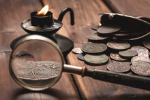 Old Ancient Coins And Magnifying Glass On The Brown Wooden Table Background