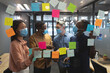 © Wavebreak Media - Diverse office colleagues wearing face masks discussing over memo notes on glass board at modern off