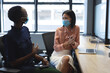© Wavebreak Media - African american woman and asian woman wearing face masks talking to each other at modern office