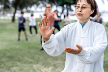 Mature Chinese Woman Do Tai Chi With Blirred Group Of People Outdoor In The Park
