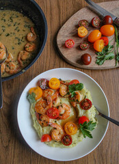 Wall Mural - Glazed shrimp with garlic and honey sauce over creamy mashed potatoes and topped with colourful cherry tomatoes and coriander leaves. Beautiful spring meal plated on wooden table. 