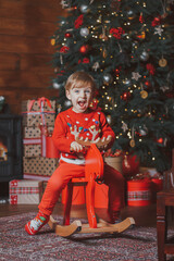 Wall Mural - a boy in a New Year's sweater and a santa claus hat under a big tree looks at gifts