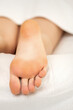 © okskukuruza - Closeup of sole of a young woman lying in bed under a white carpet