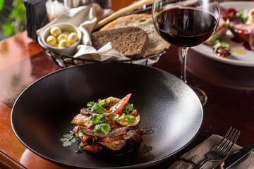 Warm salad with grilled veal, tomato, eggplant and glass of red wine on the table at restaurant