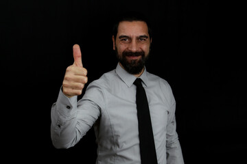 A businessman in a shirt and tie with a smiling face on a black background makes the thumb up gesture. Business concept