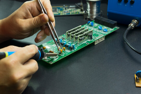 An electronics technician repairs components of a computer circuit board. Complex work with a soldering station on a table.