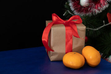 A gift wrapped in craft paper with a red wide ribbon stands on a blue table near the Christmas tree. Holidays.