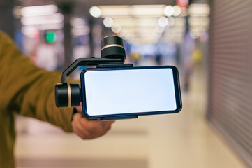 Wall Mural - A man holds a smartphone with a stabilizer in his hand. Blogger in the mall.