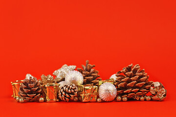 Wall Mural - Christmas arrangement with golden tree bauble ornaments, gift boxes and fir cones on bright red background with empty copy space