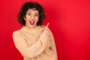 Sticker - Young beautiful Arab woman wearing beige sweater against red background pointing away and smiling to you. Look over there!