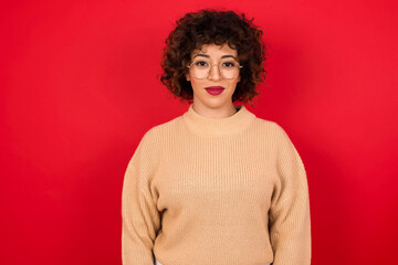 Sticker - Happy Young beautiful Arab woman wearing beige sweater against red background looking at camera with charming cute smile.