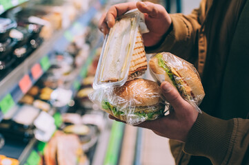 Wall Mural - A man in a supermarket holds a burger and a sandwich.