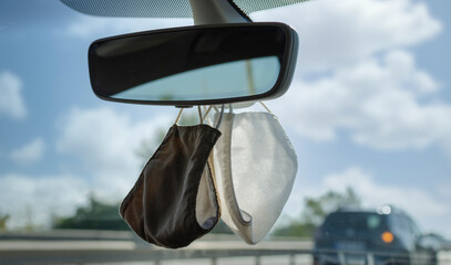 Two protective mask hanging from te rear view mirror of a car. Selective focus.  Blurry background.