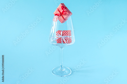 Glass wine glass with red gift boxes inside on a blue background. Romantic minimalistic Christmas background. Layout for greeting cards and greetings. Copy space