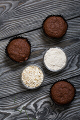 Wall Mural - Oatmeal chocolate muffins. Drawn up on a silver platter. One is broken to show a cut. Nearby are cereals and oat flour. On black pine boards.