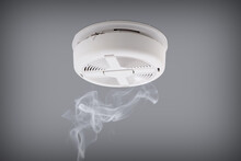 Smoke Detector Installed On A Ceiling With Rising Smoke Underneath