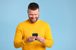 © JenkoAtaman - funny cheerful  man in a yellow sweater with phone on blue background