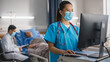 © Gorodenkoff - Hospital Ward: Professional Experienced Chinese Head Nurse / Doctor Wearing Face Mask Uses Medical Touch Screen Computer, Checking Patient's Medical Data. In the Background Patient Recovering on Bed.