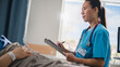 © Gorodenkoff - Hospital Ward: Portrait of Friendly Chinese Head Nurse Talks to Anonymous Patient Recovering in Bed and Fills Medical History Form. Doctor Helps Person Get Better. Dutch Angle Shot.