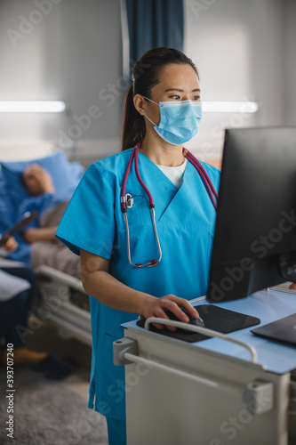 Hospital Ward: Vertical Portrait Shot of a Professional Experienced Chinese Head Nurse / Doctor Wearing Face Mask Uses Medical Touch Screen Computer, Checking Patient\'s Medical Data, Treatment Plan.