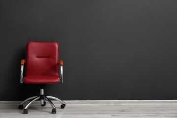 Comfortable office chair near black wall indoors. Space for text