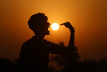 Optical Illusion Of Silhouette Man Eating Sun In Sky During Sunset