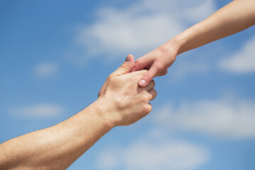 Wall Mural - Hands of man and woman reaching to each other, support. Solidarity, compassion, and charity, rescue. Giving a helping hand. Hands of man and woman on blue sky background. Lending a helping hand